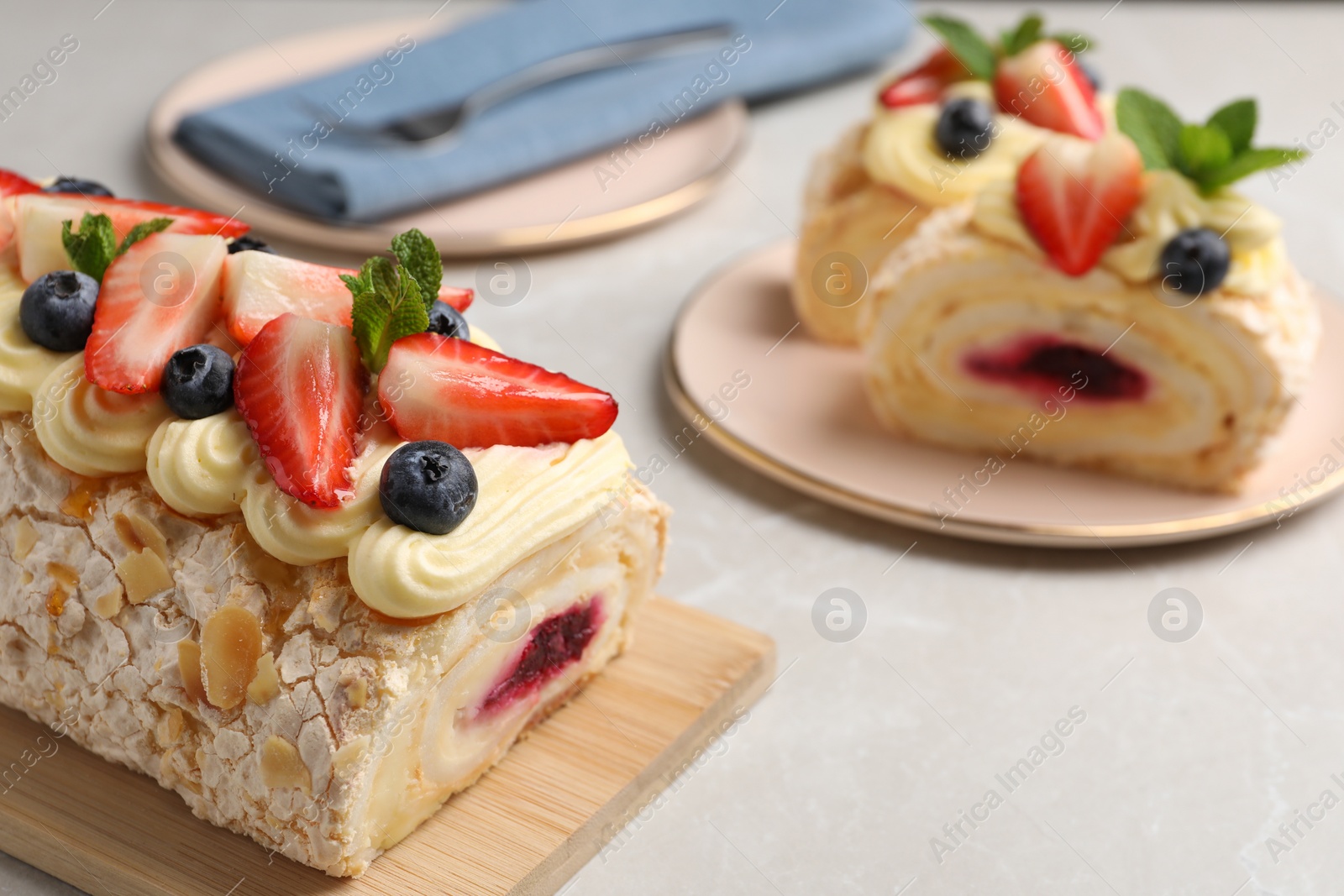 Photo of Tasty meringue roll with jam, cream, strawberry, blueberry and mint on light grey marble table, closeup