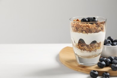 Photo of Yogurt served with granola and blueberries on white wooden table, space for text