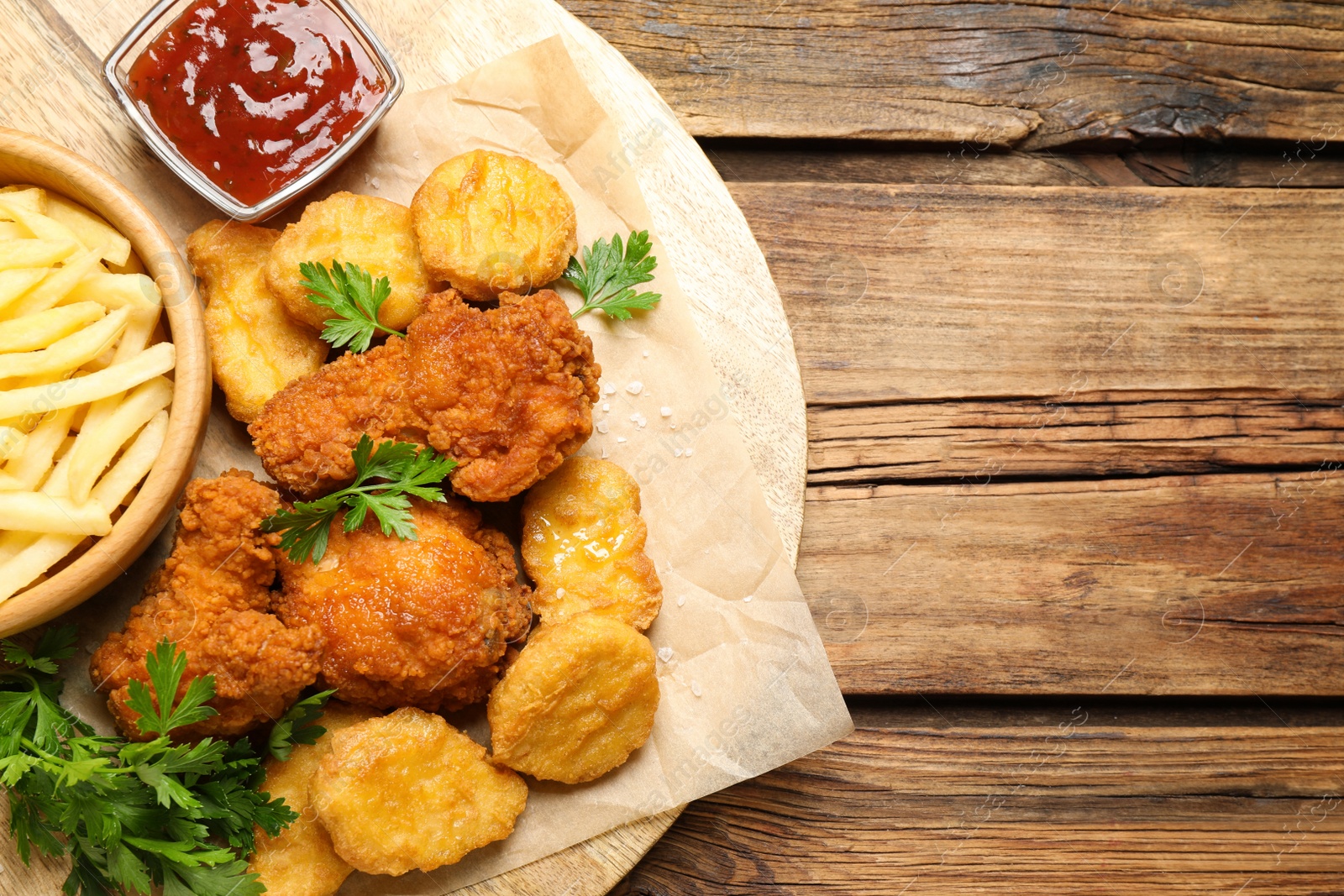 Photo of Tasty fried chicken nuggets with garnish on wooden table, top view. Space for text