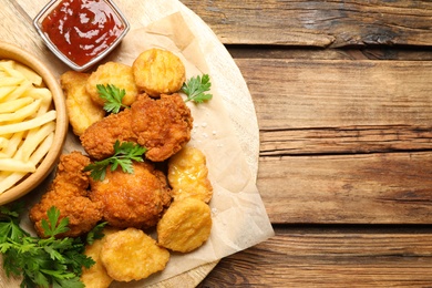 Tasty fried chicken nuggets with garnish on wooden table, top view. Space for text