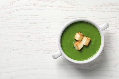 Photo of Fresh vegetable detox soup with croutons in dish and space for text on wooden background, top view