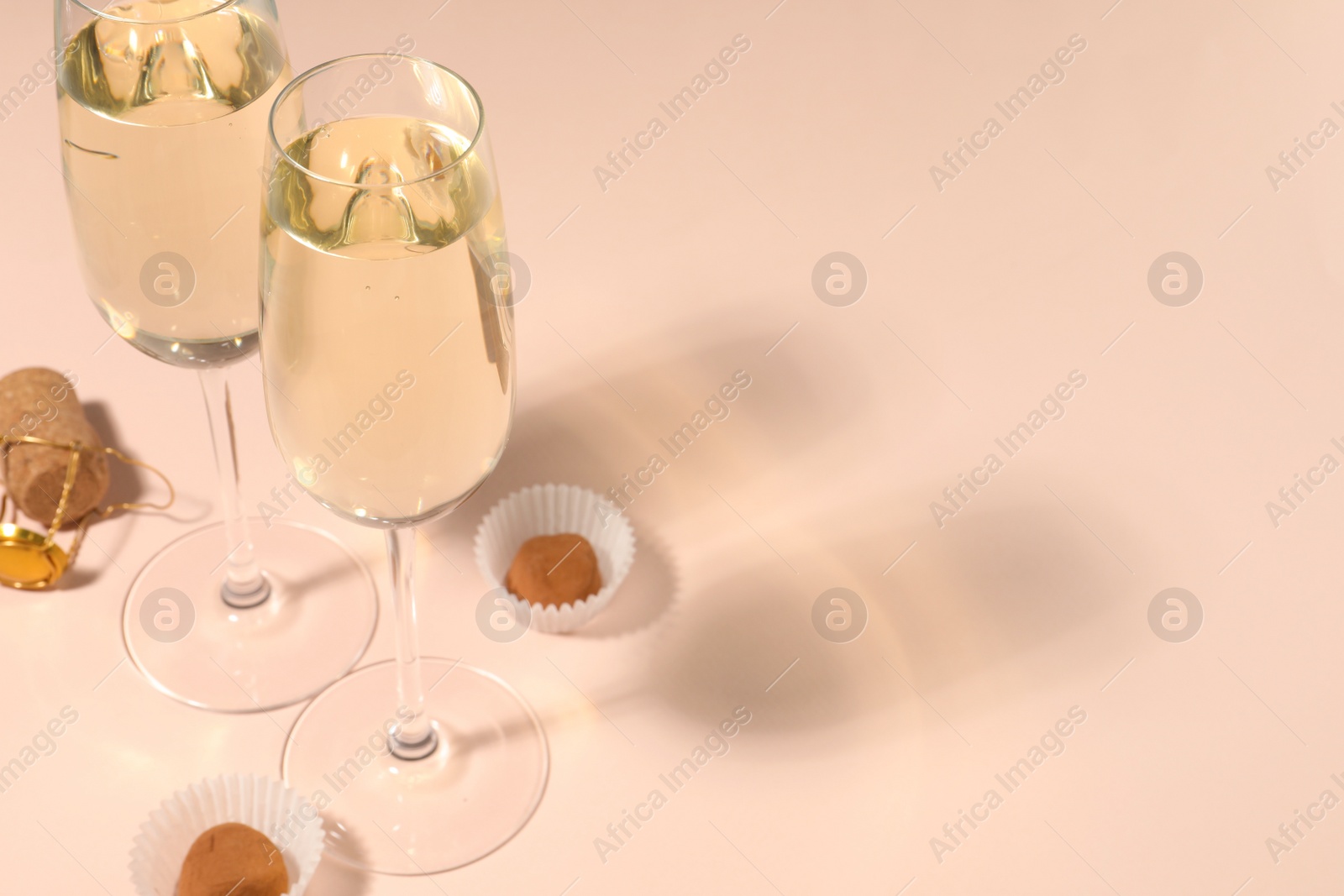 Photo of Glasses of delicious sparkling wine and chocolate truffles on pale pink background. Space for text