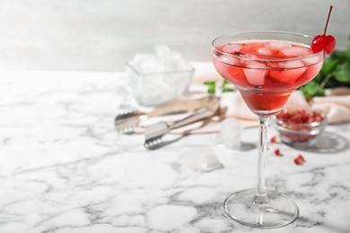 Glass of delicious cocktail with ice and cherry on white marble table. Space for text