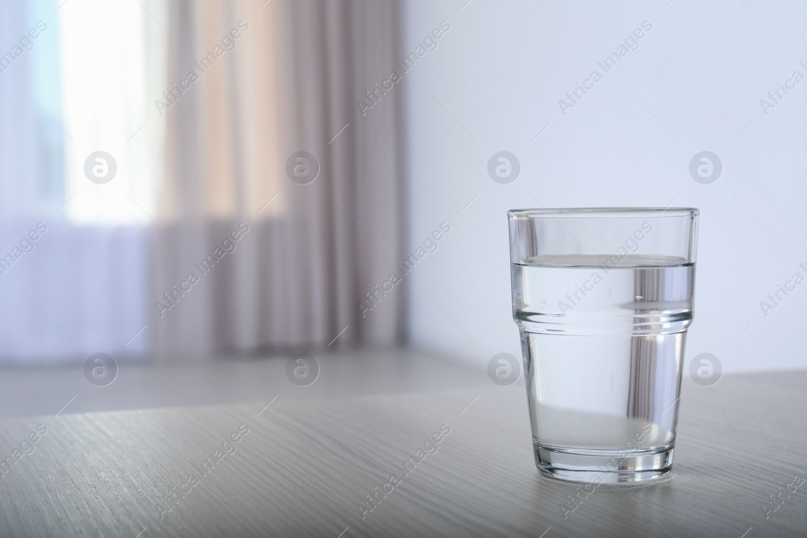 Photo of Glass of water on table against blurred background. Space for text