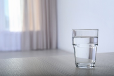 Photo of Glass of water on table against blurred background. Space for text