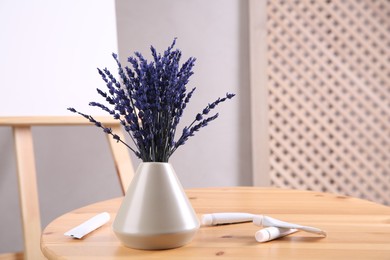 Bouquet of beautiful preserved lavender flowers and paints on wooden table near easel indoors, closeup