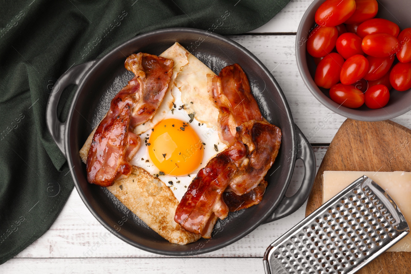 Photo of Delicious crepe with egg and bacon in dish on white wooden table, flat lay. Breton galette