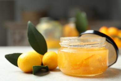 Photo of Delicious kumquat jam in jar and fresh fruits on white table, closeup