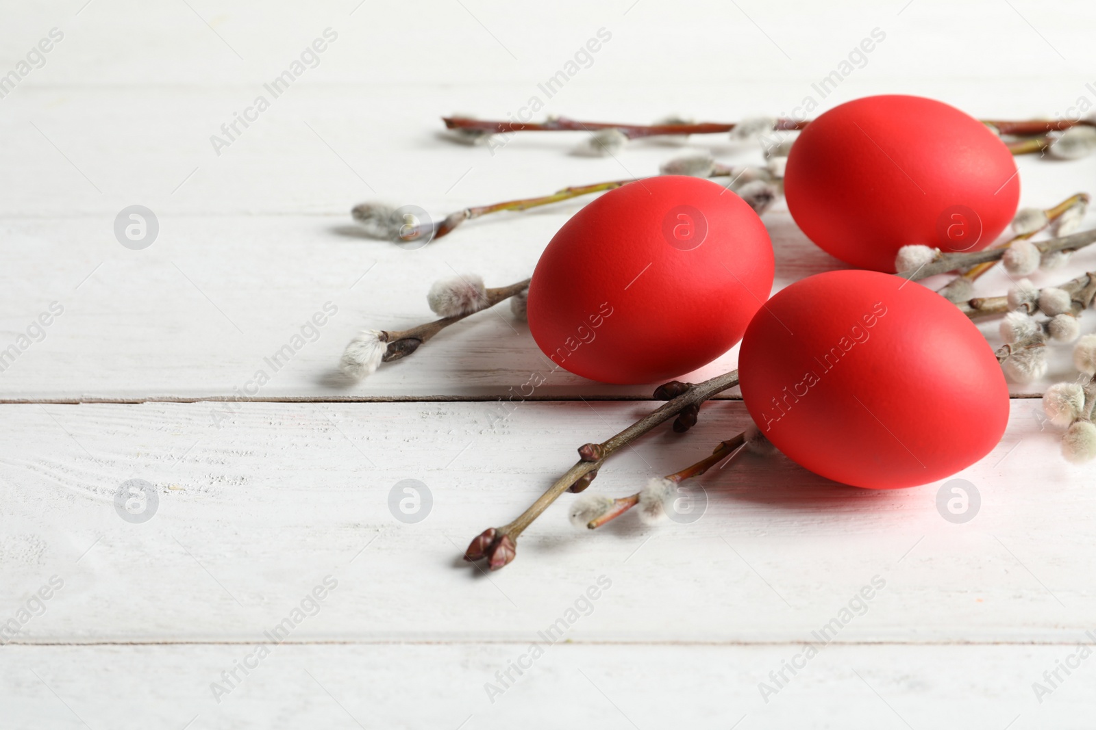 Photo of Red dyed Easter eggs and pussy willow on wooden table, space for text