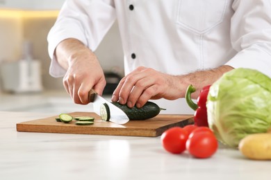 Photo of Chef cutting cucumber at marble table in kitchen, closeup