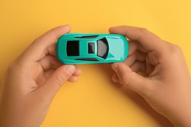 Photo of Child holding toy car on yellow background, top view