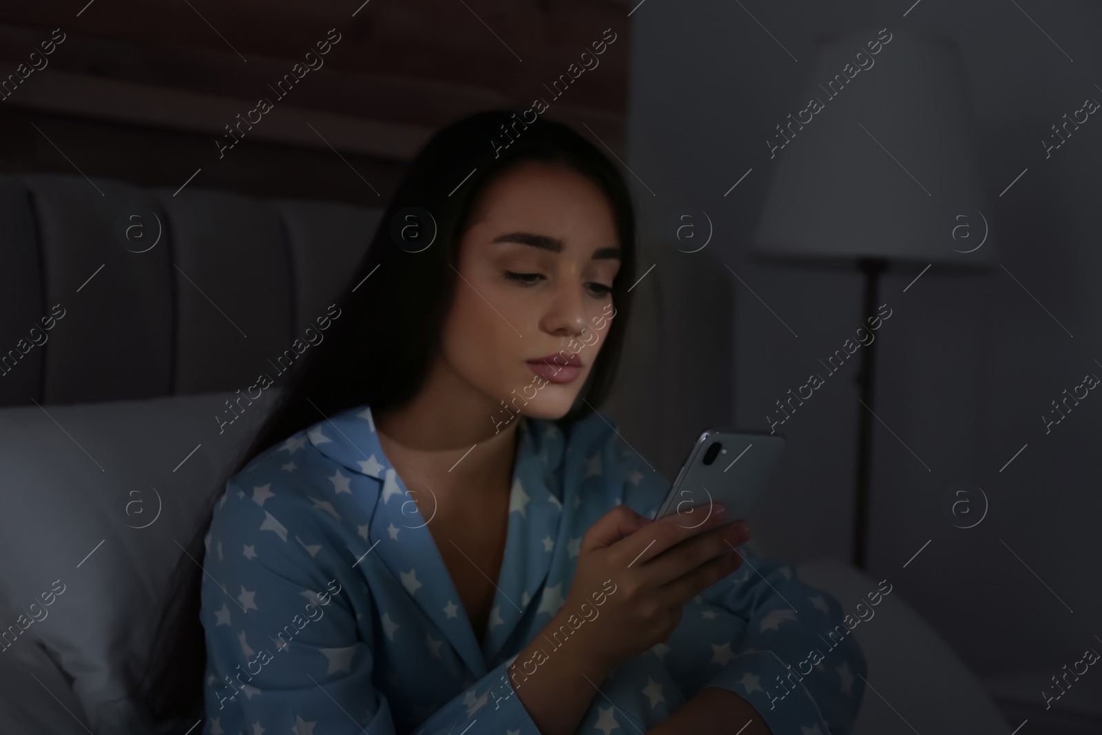 Photo of Young woman using mobile phone in dark bedroom