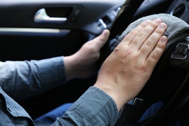 Photo of Man cleaning steering wheel with rag in car, closeup