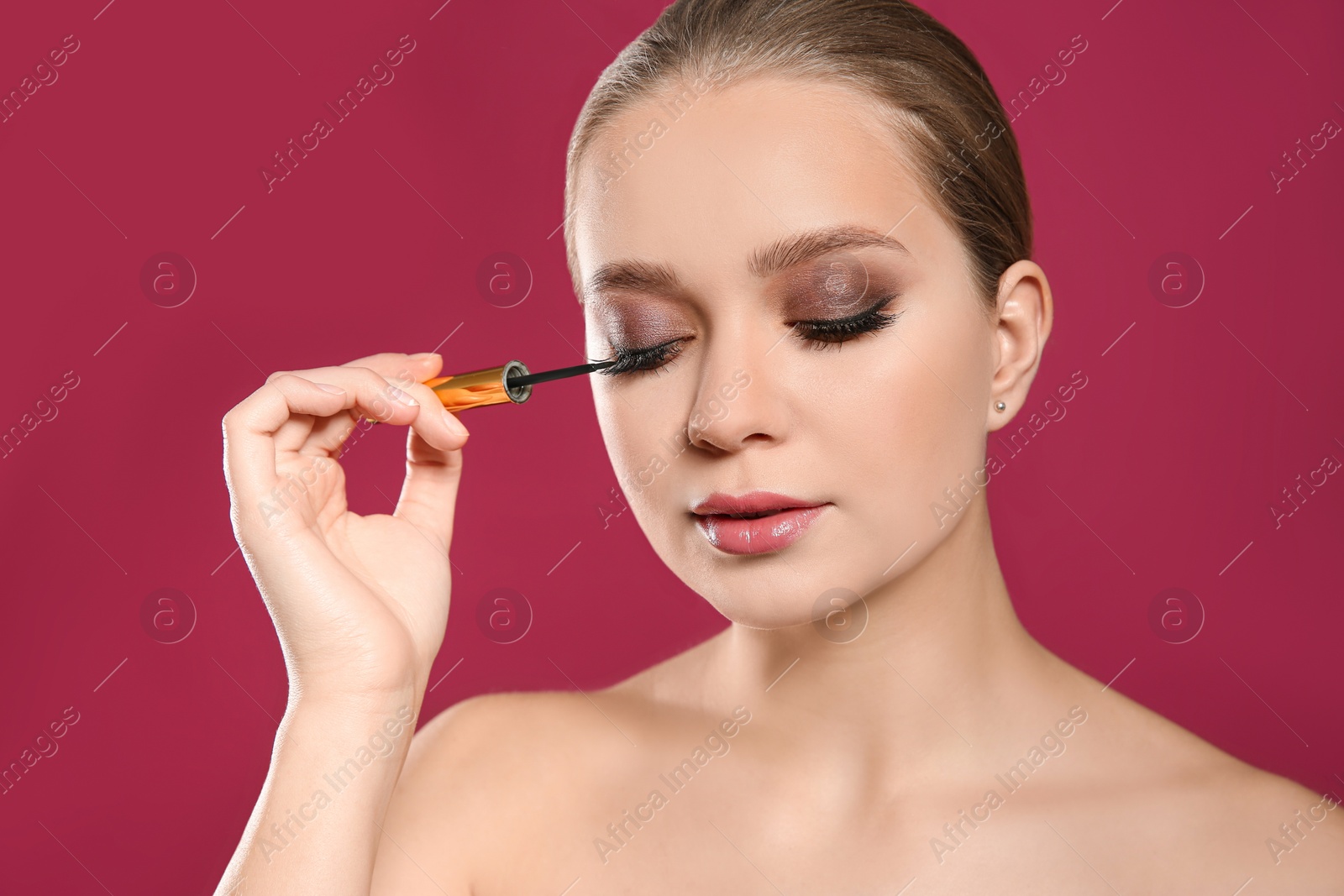 Photo of Beautiful woman applying eyeliner on pink background. Stylish makeup