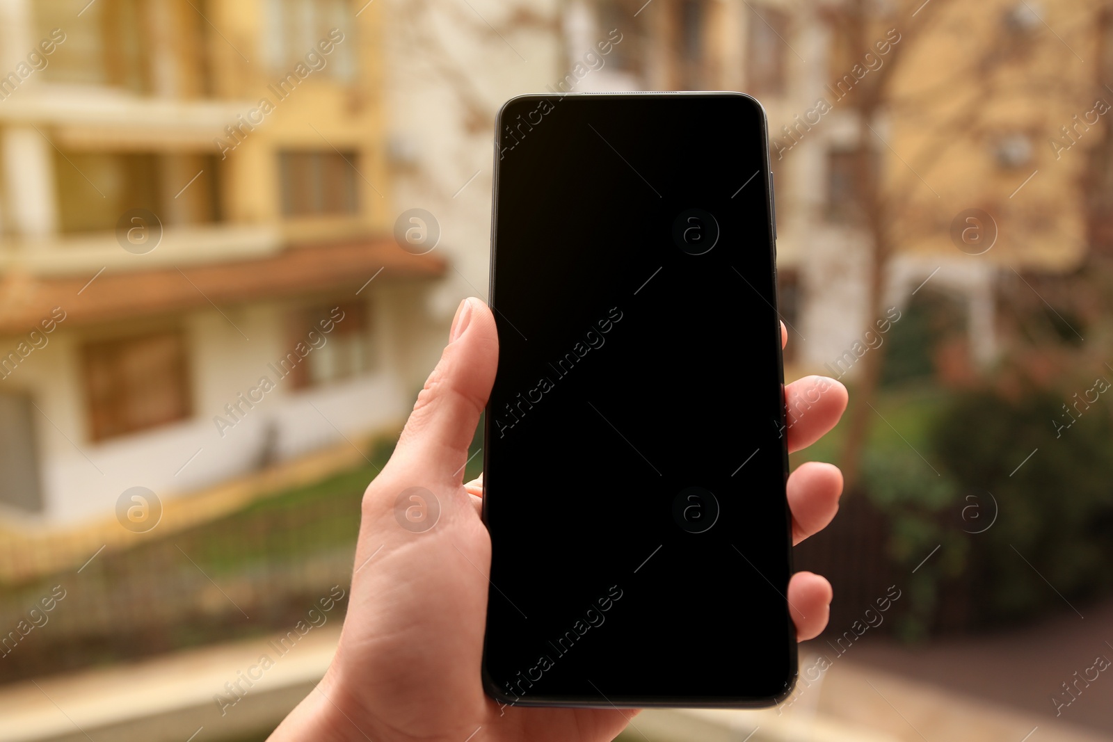 Photo of Woman holding smartphone with blank screen near building outdoors, closeup