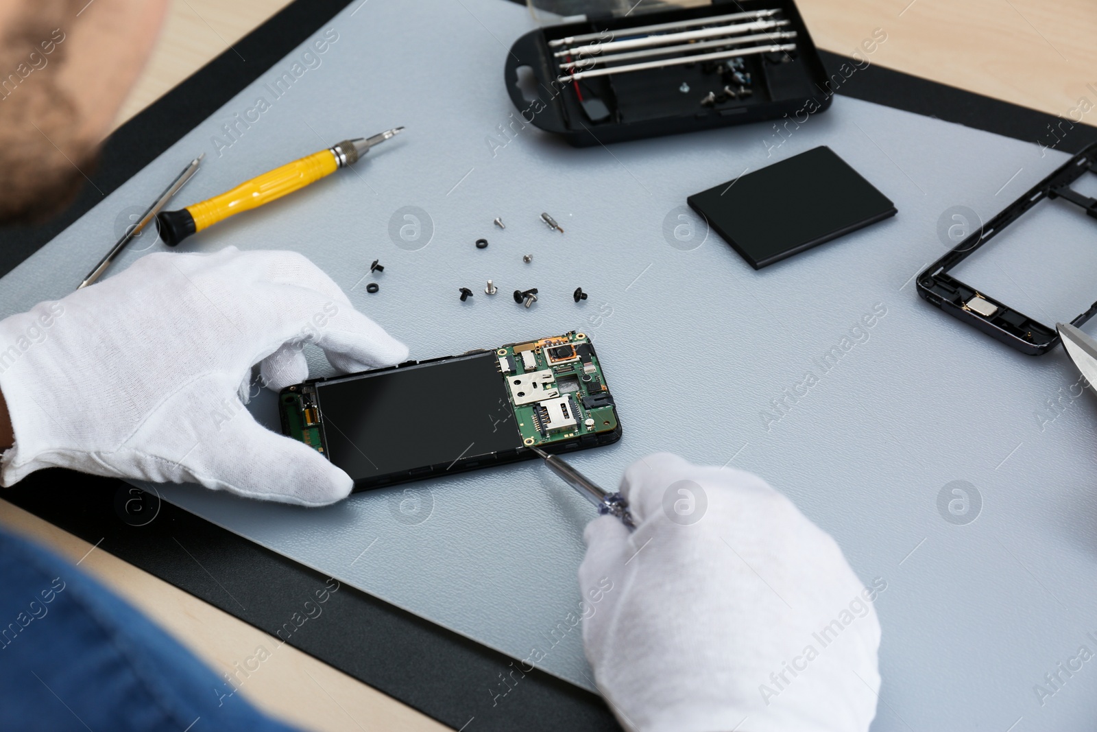 Photo of Technician repairing broken smartphone at table, closeup