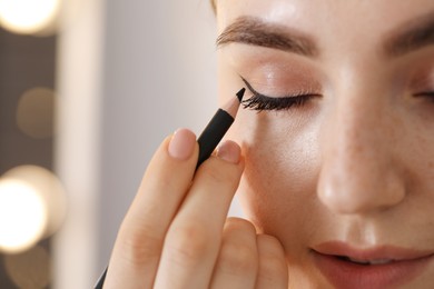 Photo of Makeup product. Woman applying black eyeliner indoors, closeup