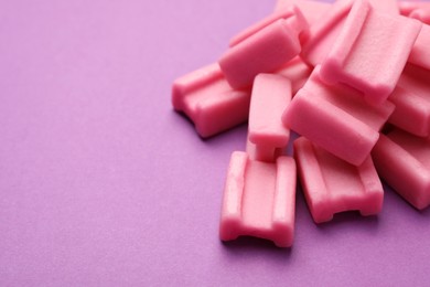 Photo of Tasty pink chewing gums on purple background, closeup. Space for text