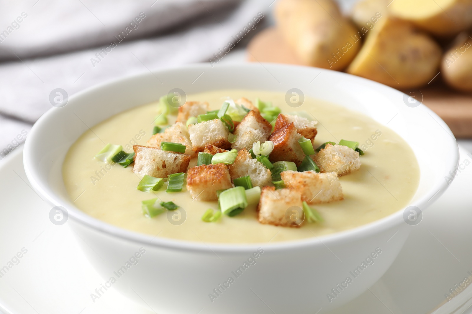 Photo of Tasty potato soup with croutons and green onion in bowl on white table, closeup