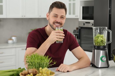 Happy man drinking delicious smoothie at white marble table in kitchen