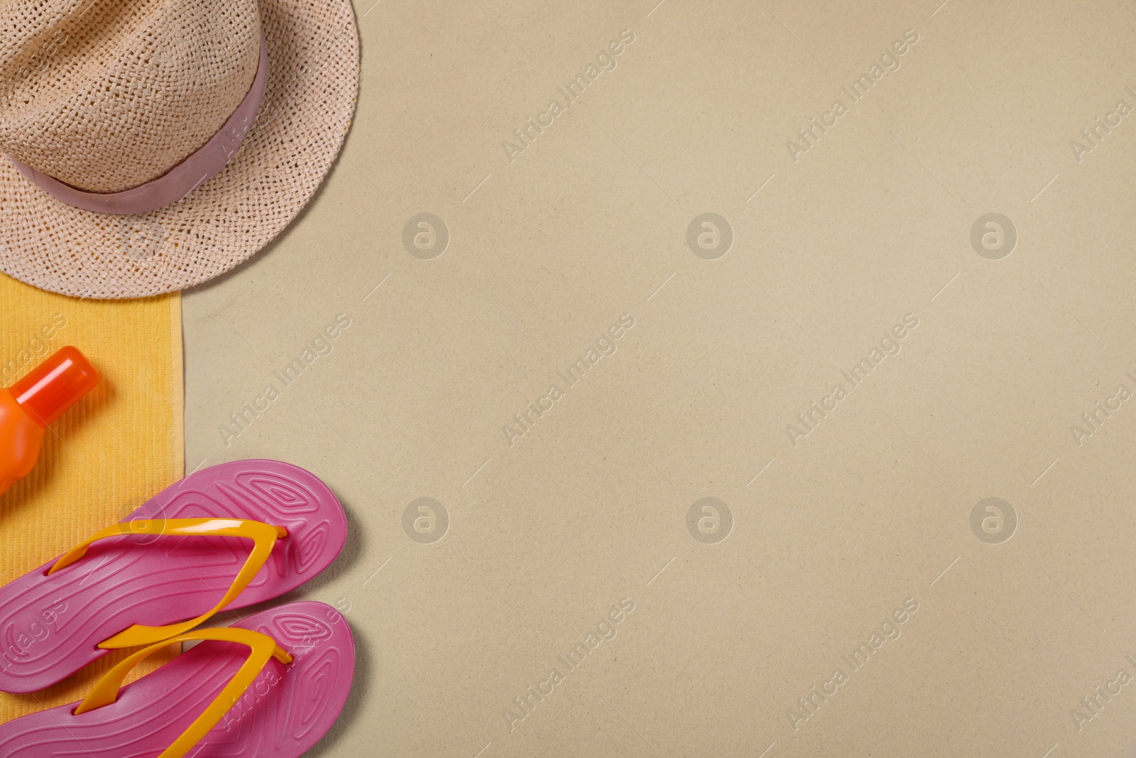 Photo of Beach towel, hat, sunscreen and flip flops on sand, flat lay. Space for text