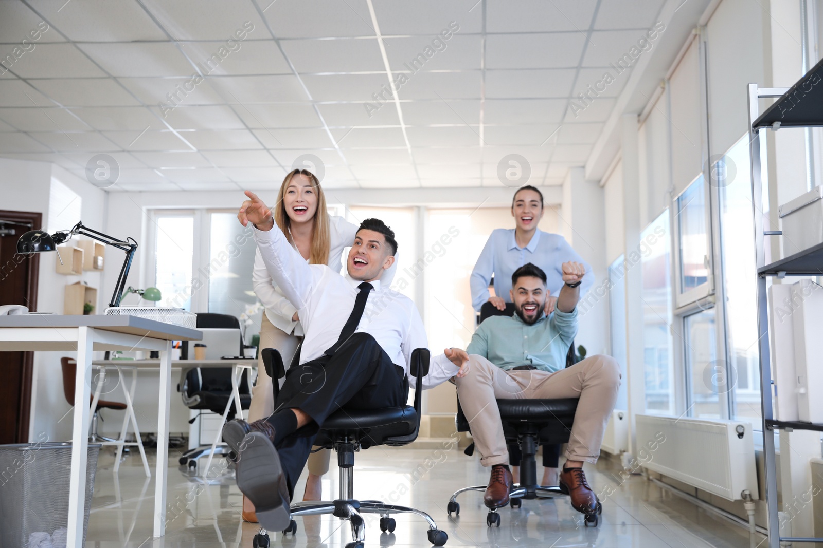 Photo of Happy office employees riding chairs at workplace