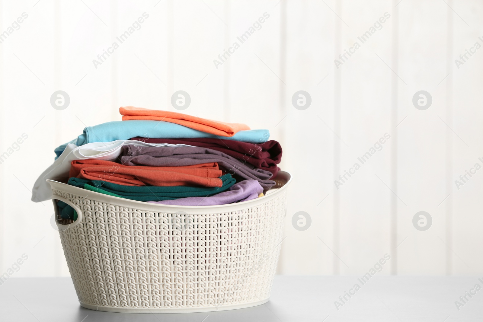 Photo of Basket with clean laundry on table against light background, space for text