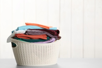 Basket with clean laundry on table against light background, space for text