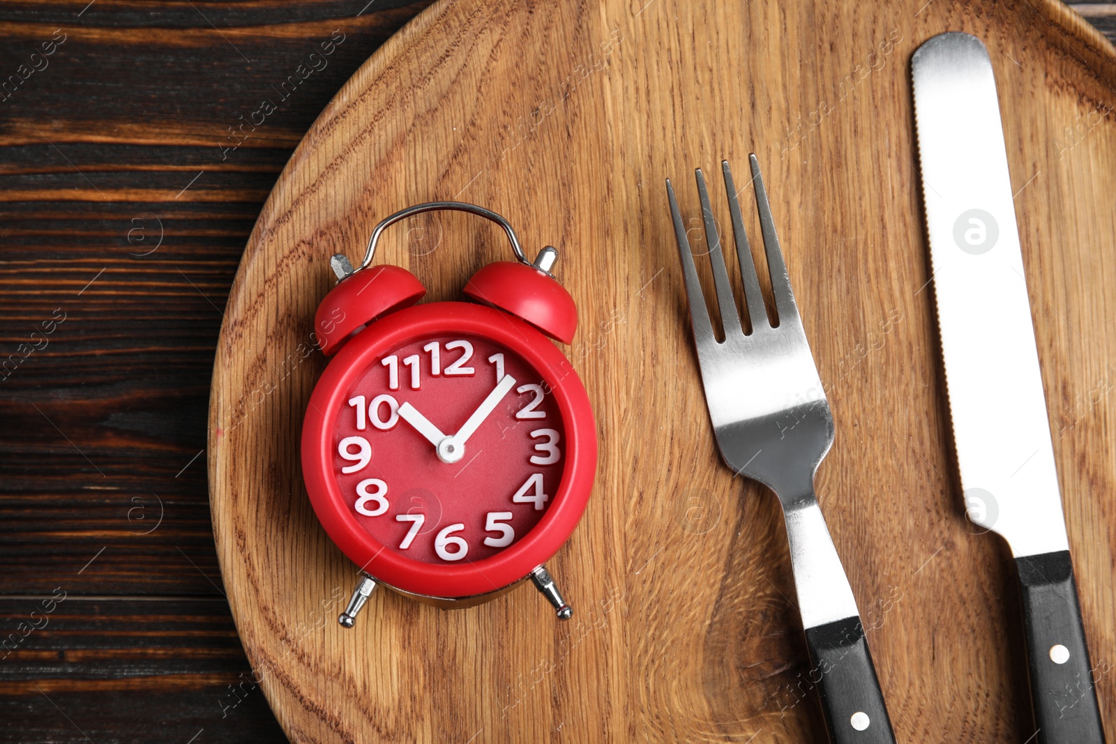 Photo of Alarm clock and cutlery in plate on wooden table, top view. Diet regime