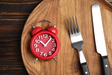 Photo of Alarm clock and cutlery in plate on wooden table, top view. Diet regime