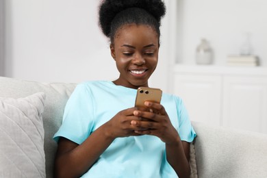 Photo of Happy young woman using smartphone on sofa at home