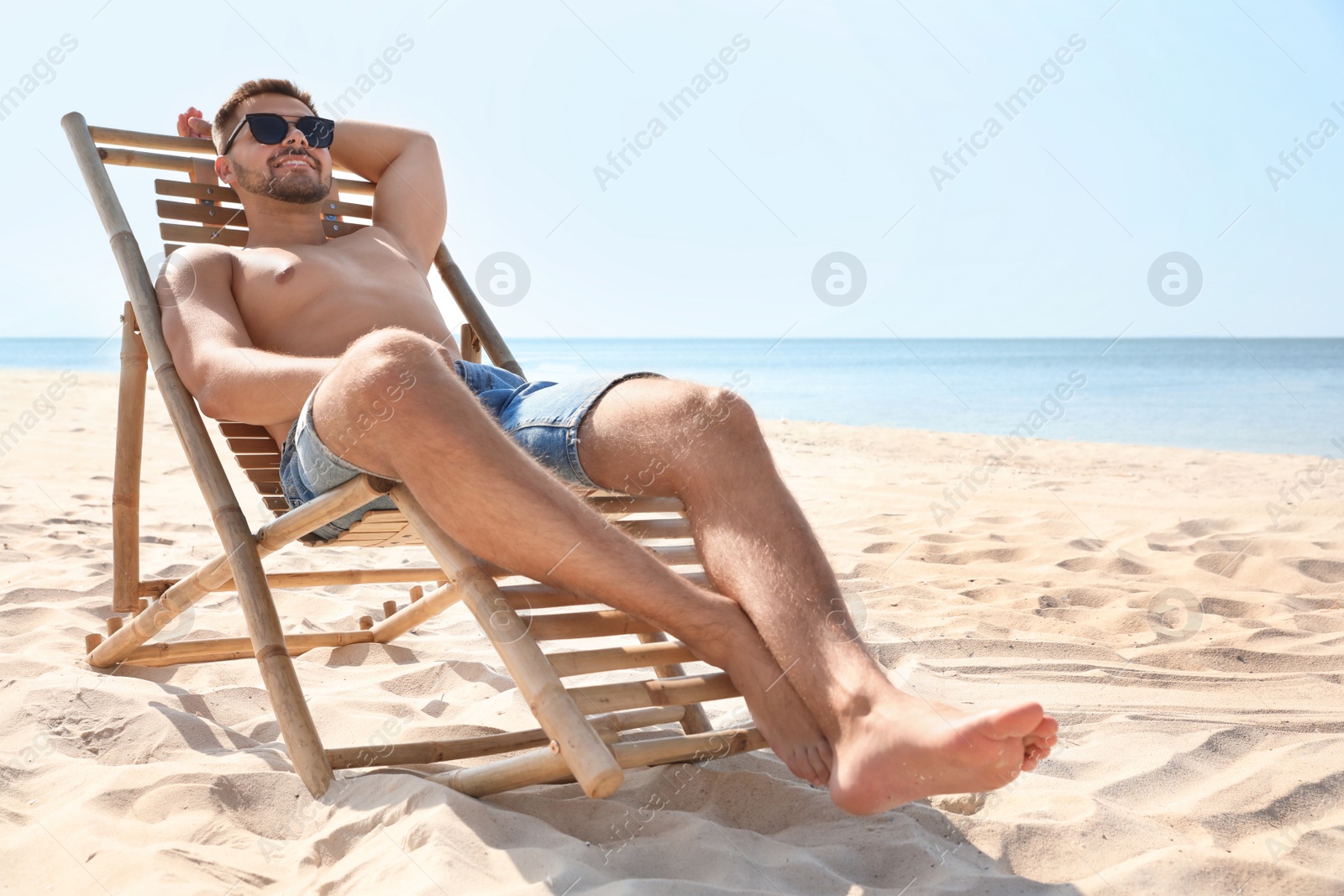 Photo of Young man relaxing in deck chair on sandy beach