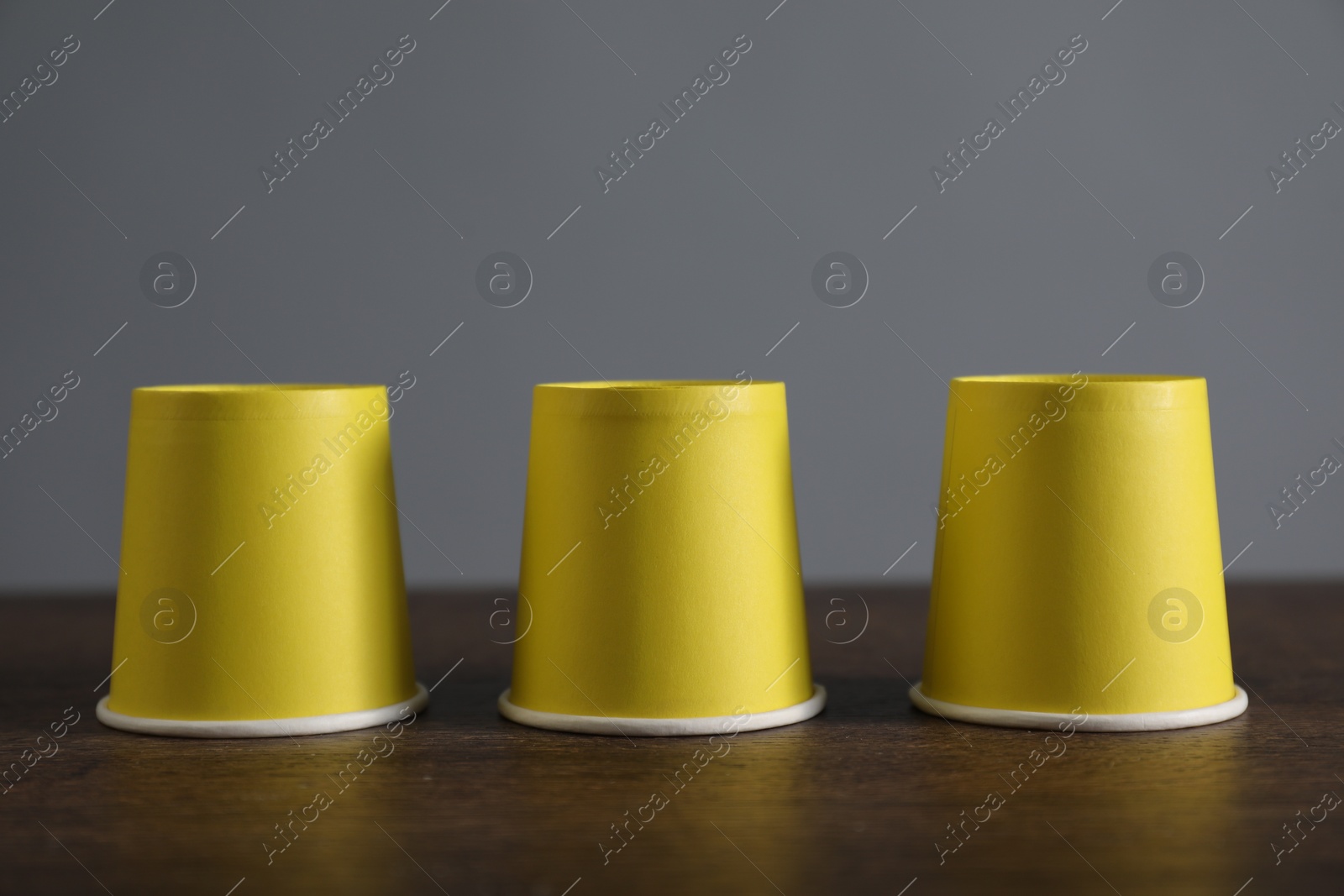 Photo of Shell game. Three yellow cups on wooden table