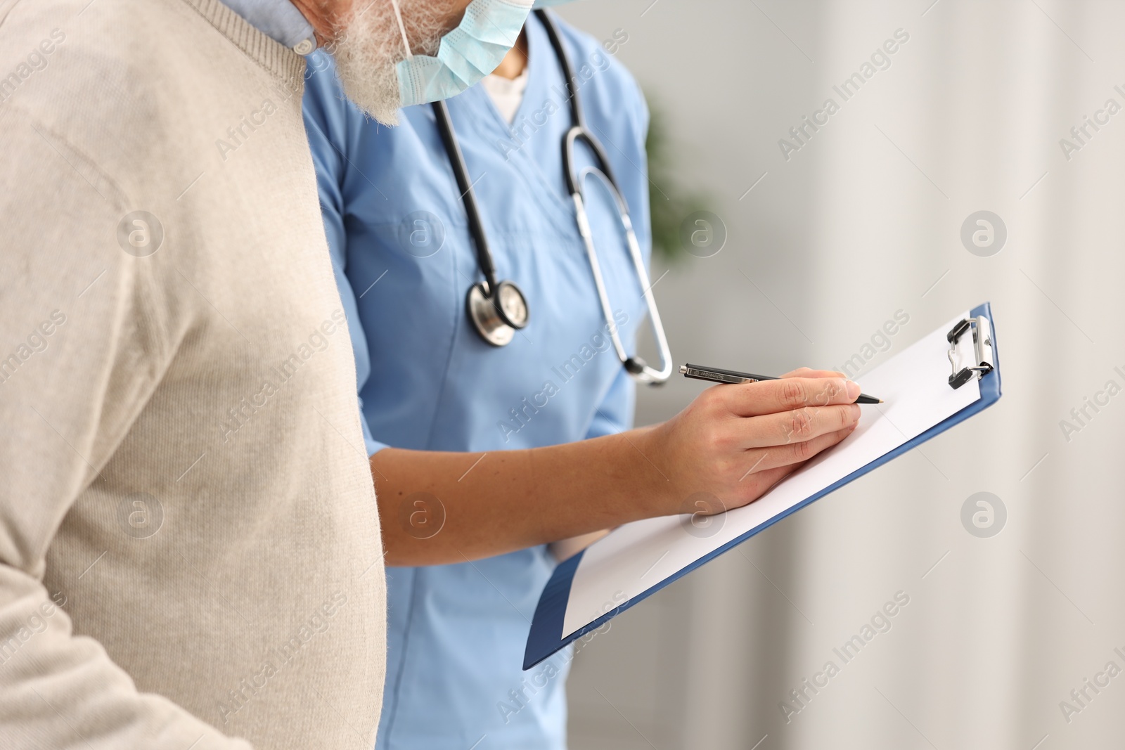 Photo of Nurse with clipboard and elderly patient indoors, closeup
