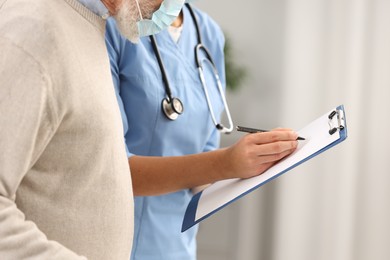 Nurse with clipboard and elderly patient indoors, closeup