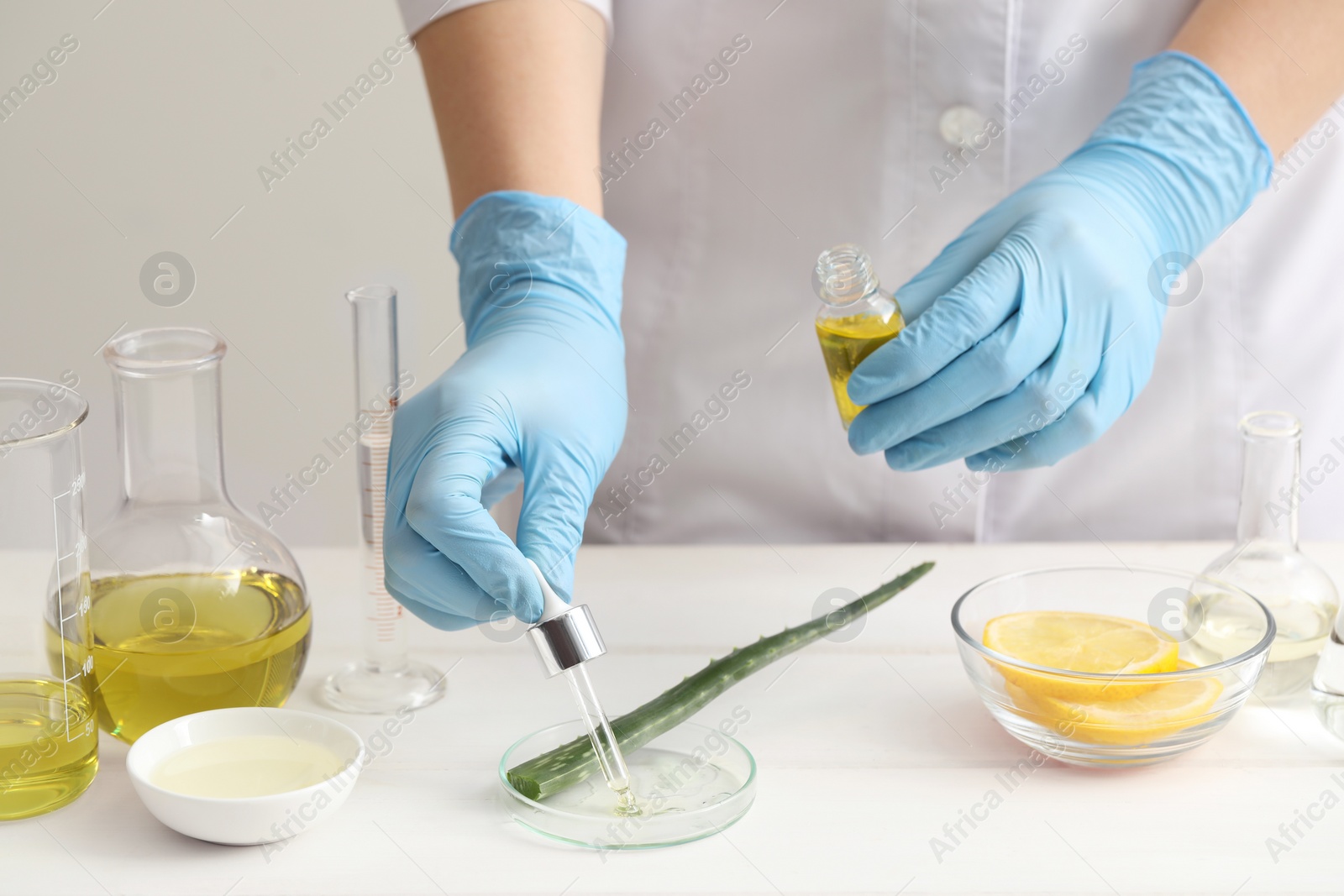 Photo of Scientist developing cosmetic oil at white table, closeup