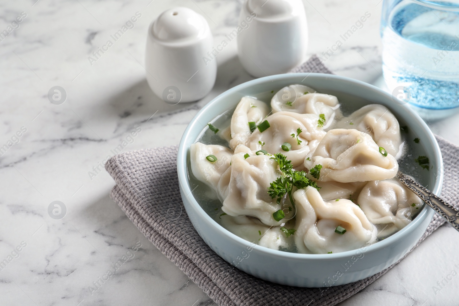 Photo of Bowl of tasty dumplings in broth with spoon on white marble table. Space for text