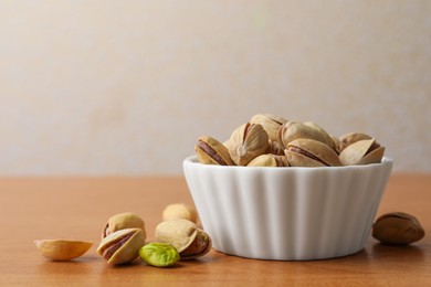 Bowl and pistachio nuts on wooden table, closeup