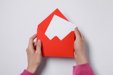 Woman holding letter envelope with card at white table, top view. Space for text