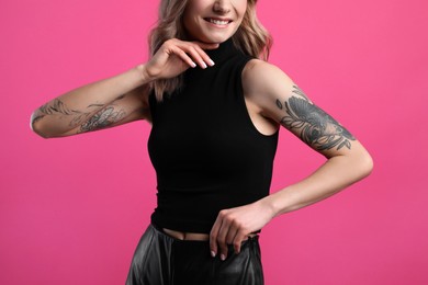 Photo of Beautiful woman with tattoos on arms against pink background, closeup