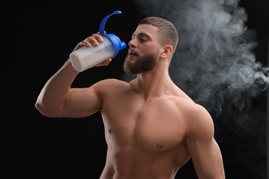 Young man with muscular body drinking protein shake on black background