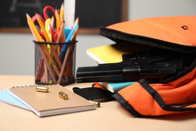 Photo of Gun, bullets and school stationery on wooden table indoors, closeup