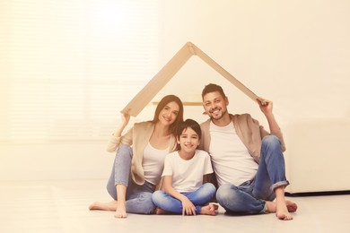 Image of Happy family sitting under cardboard roof at home. Insurance concept