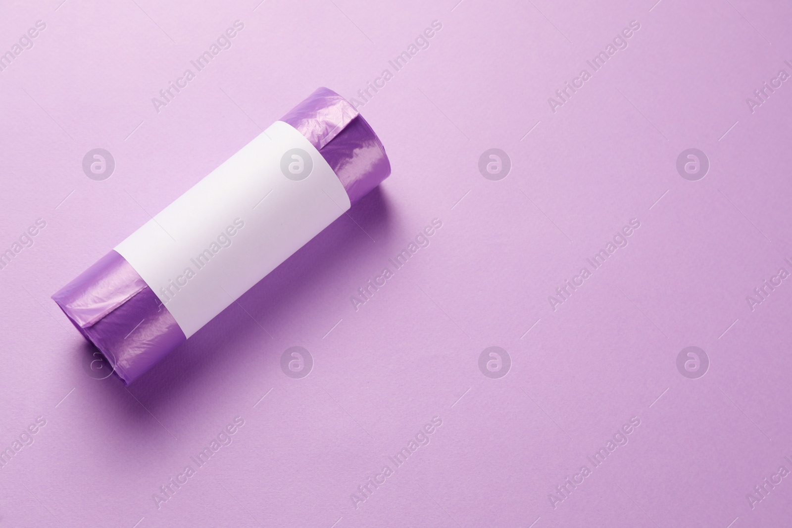 Photo of Roll of violet garbage bags on color background, top view. Space for text