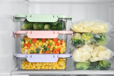 Plastic bags and containers with different frozen vegetables in refrigerator