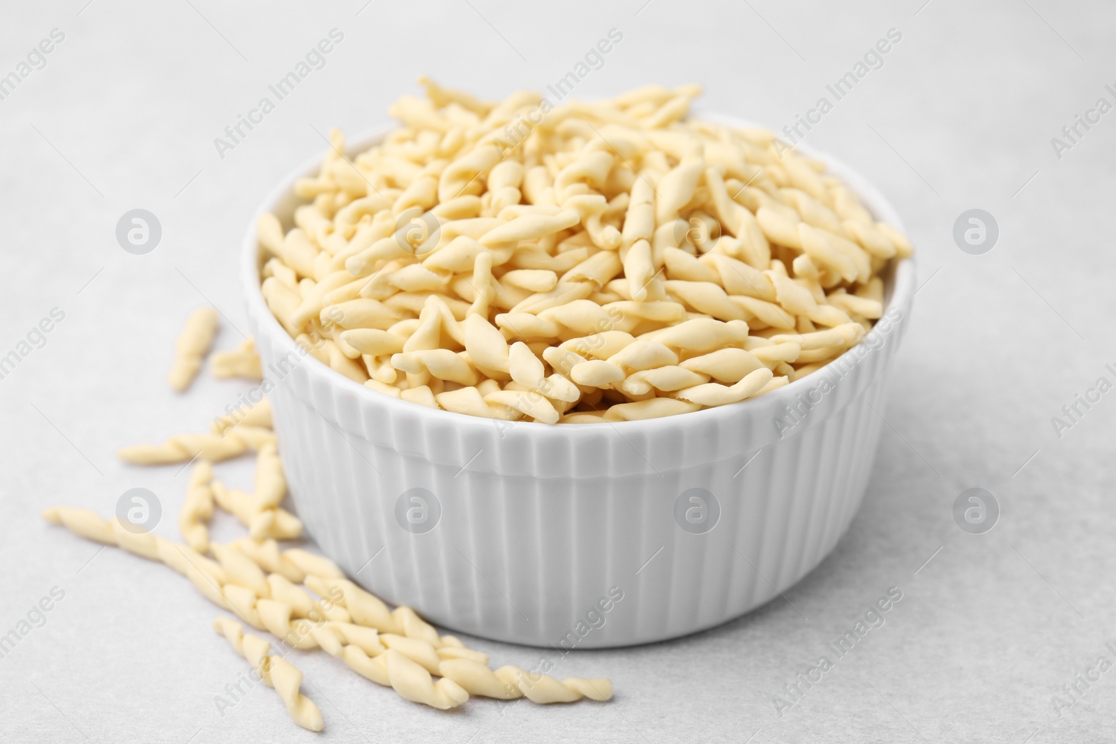 Photo of Bowl with uncooked trofie pasta on light grey table, closeup