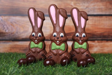 Photo of Easter celebration. Funny chocolate bunnies and candies on grass against wooden background