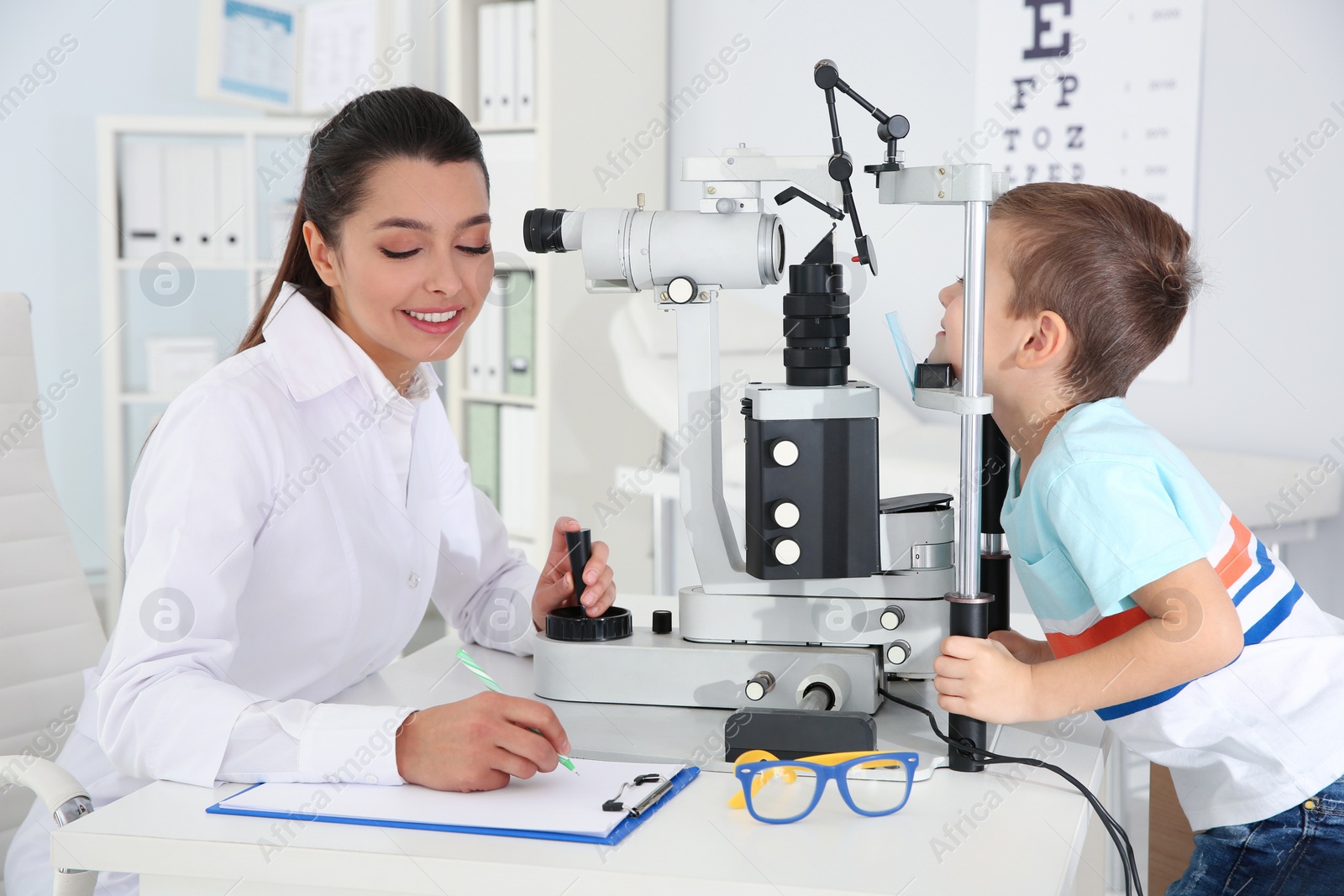 Photo of Children's doctor examining little boy with ophthalmic equipment in clinic