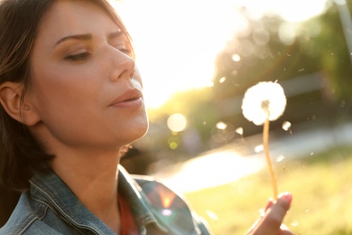 Young woman with dandelion in park on sunny day, closeup. Allergy free concept