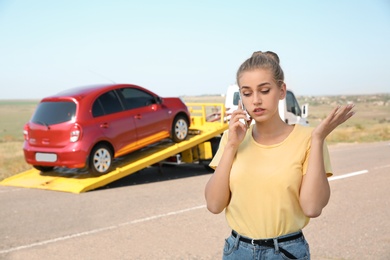 Woman talking on phone near tow truck with broken car outdoors